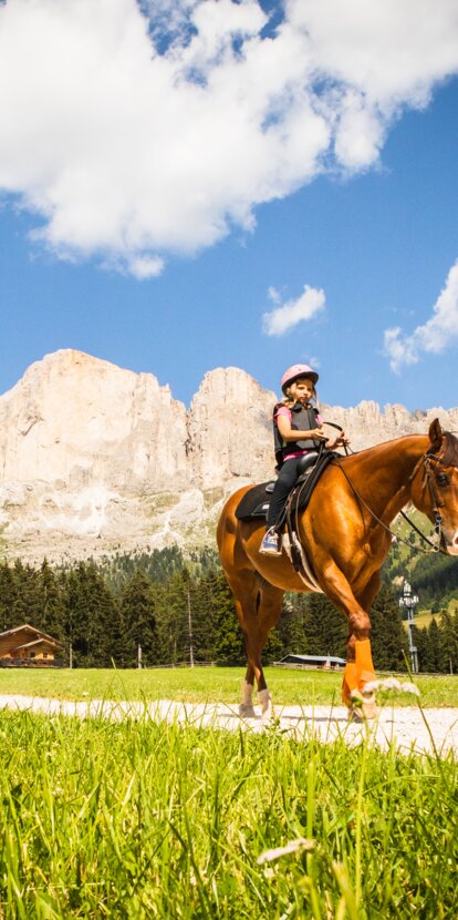 Escursioni a cavallo Angerle Alm Carezza | © Eggental Tourismus/StorytellerLabs Bambino a cavallo, cavallo marrone, vista sul Catinaccio | © Eggental Tourismus/StorytellerLabs