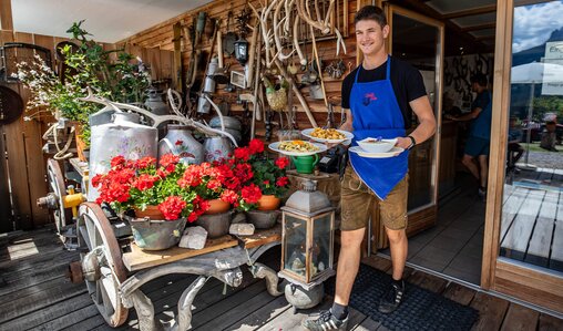 Service on the sunny terrace | © WESTSIDERS_JV A staff member serves freshly prepared dishes on a beautifully decorated sunny terrace. | © WESTSIDERS_JV
